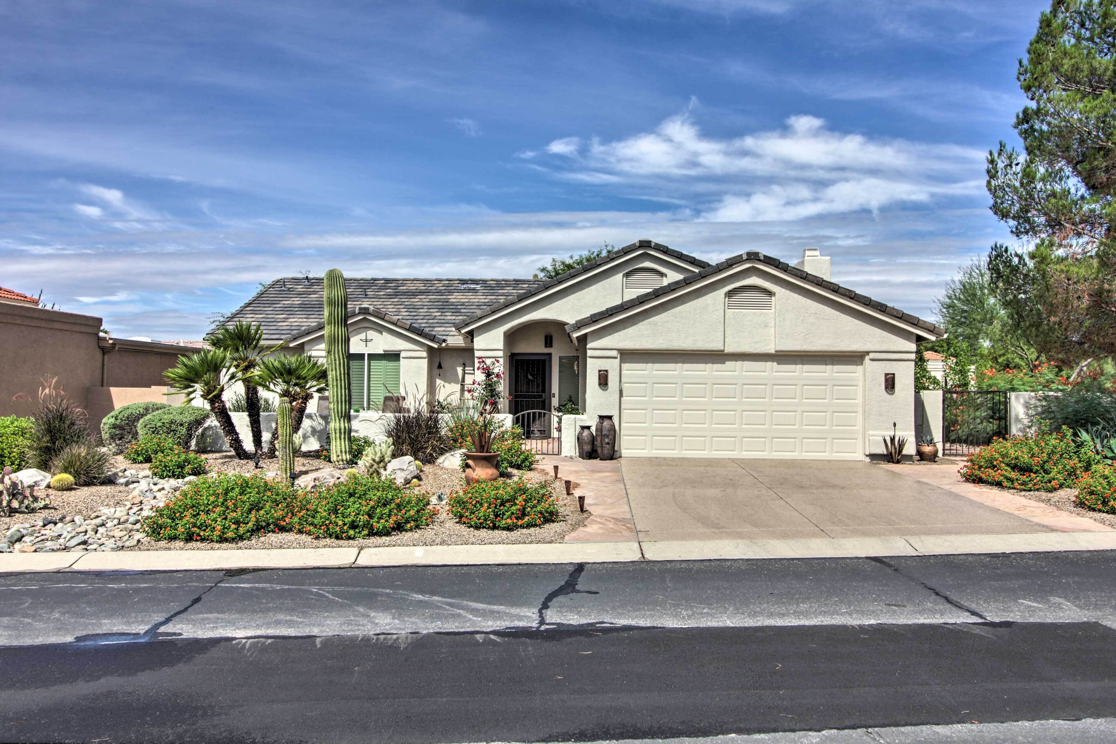 A single-story house with a garage, surrounded by a desert garden with cacti and small shrubs.
