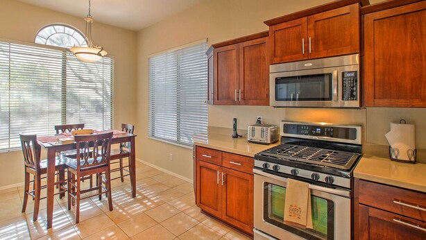 A kitchen with wooden cabinets, a stove, a microwave, and a dining table with chairs. - Scottsdale Home - Mtn Views, Pool, Near Westworld! (Scottsdale)