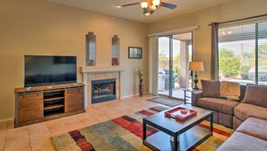 A living room with a flat-screen TV, a fireplace, a ceiling fan, and a large window. - Scottsdale Home - Mtn Views, Pool, Near Westworld! (Scottsdale)