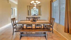 A dining room with a wooden table and benches, a chandelier, and a window with blinds. - Scottsdale Home - Mtn Views, Pool, Near Westworld! (Scottsdale)