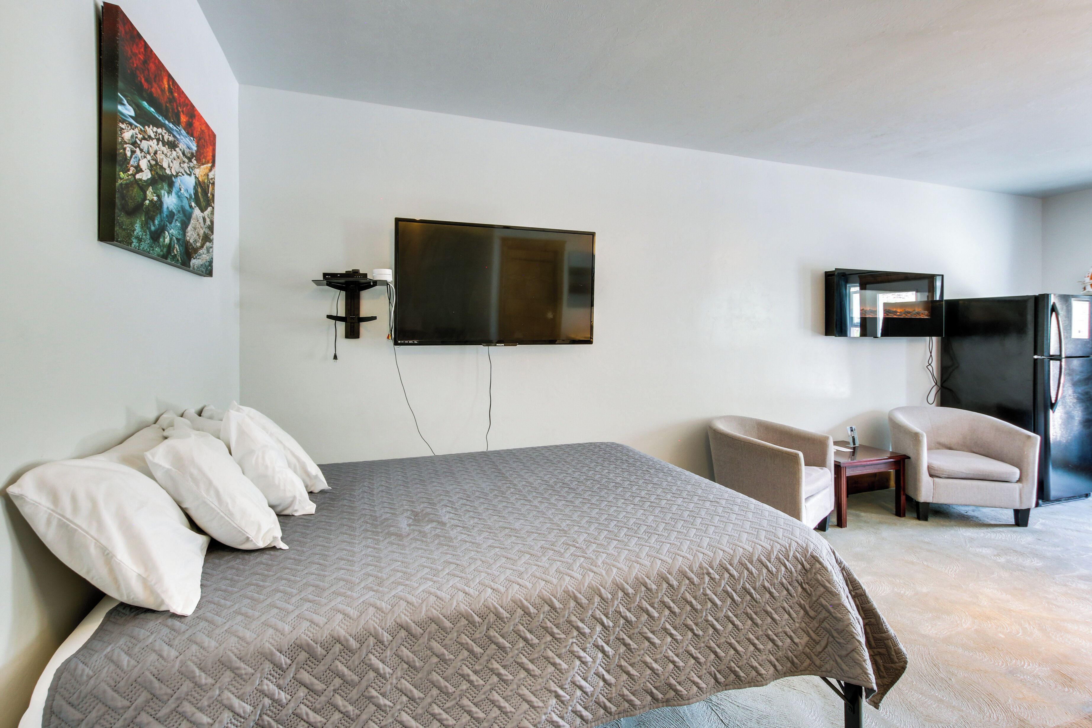 Ein Schlafzimmer mit einem Bett, einem an der Wand befestigten Fernseher, einem Kühlschrank und einem Sessel.