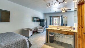 Une chambre à coucher comprenant un lit, une chaise, un bureau, une coiffeuse avec un miroir et un ventilateur de plafond.