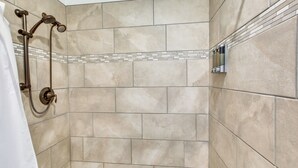 Un espace douche avec des carreaux de couleur beige et un pommeau de douche.