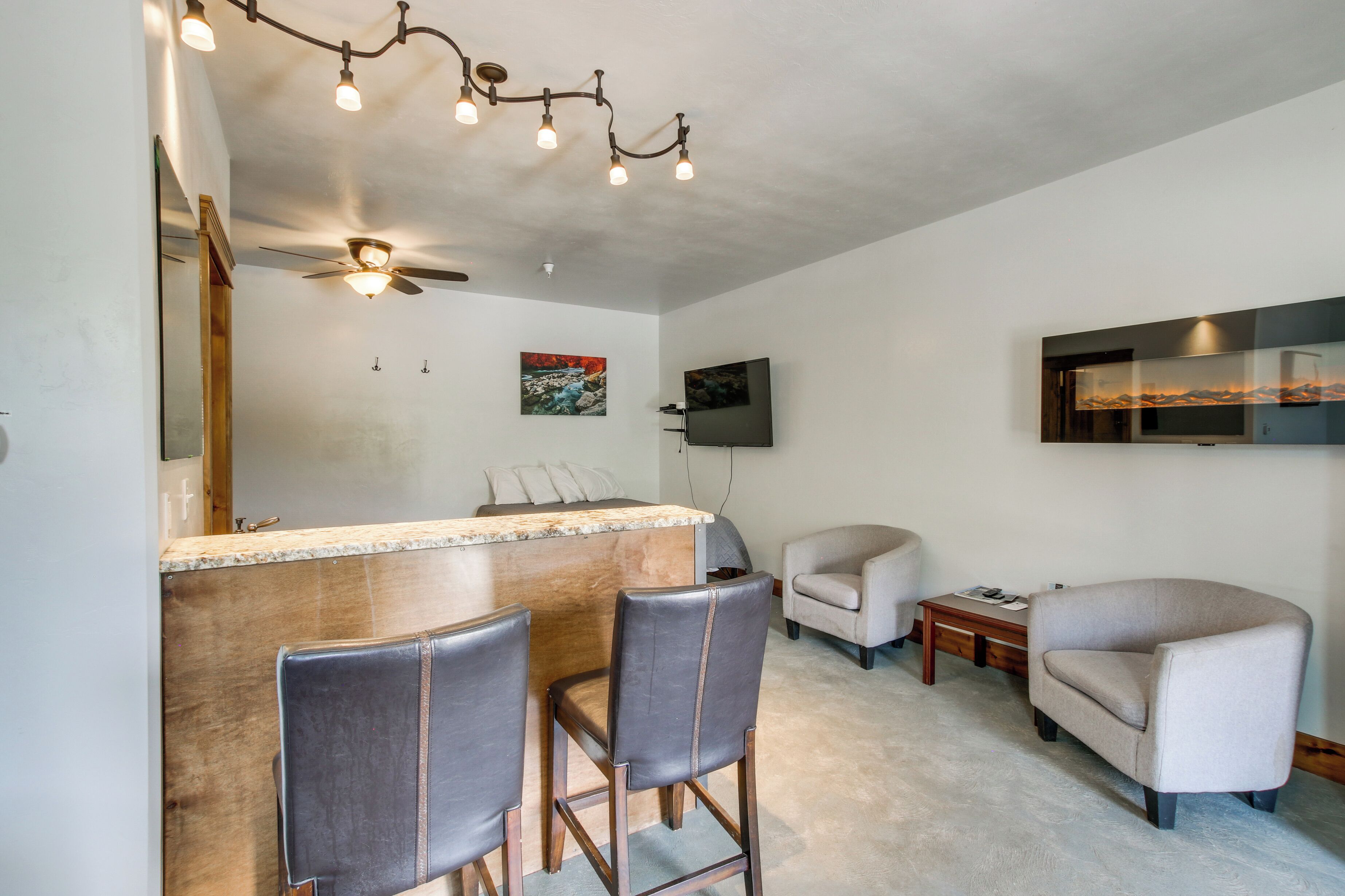Una sala de estar moderna con una zona de bar, dos sillones de cuero, un sofá, un televisor de pantalla plana y obras de arte en la pared.