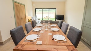 A dining area with a long wooden table set for six, surrounded by grey upholstered chairs. - 3 Bears Court Barn Conversion in Little Rissington (Cheltenham)