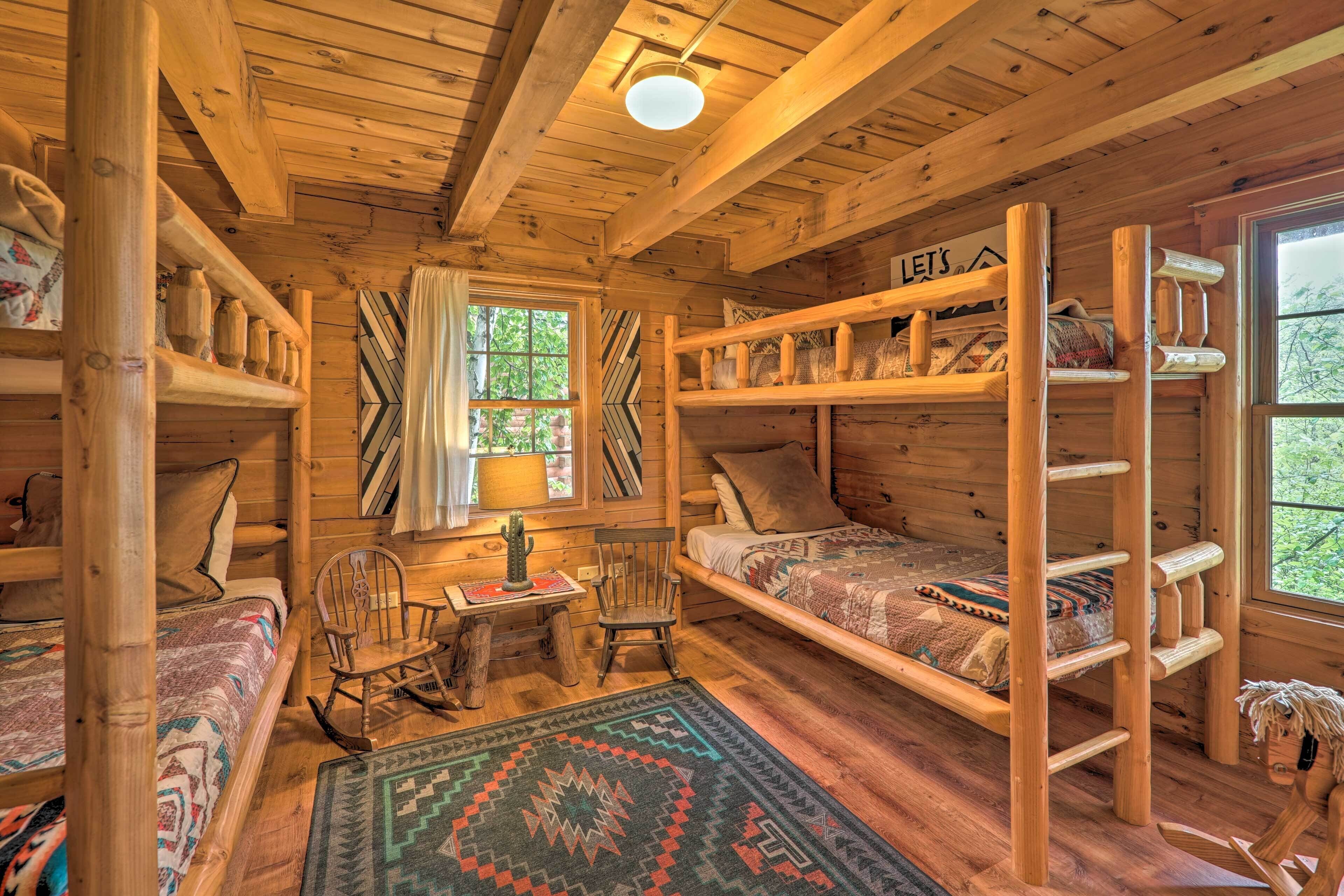 A cozy cabin with wooden walls and floors, a bunk bed, a desk with a chair, and a window with curtains.
