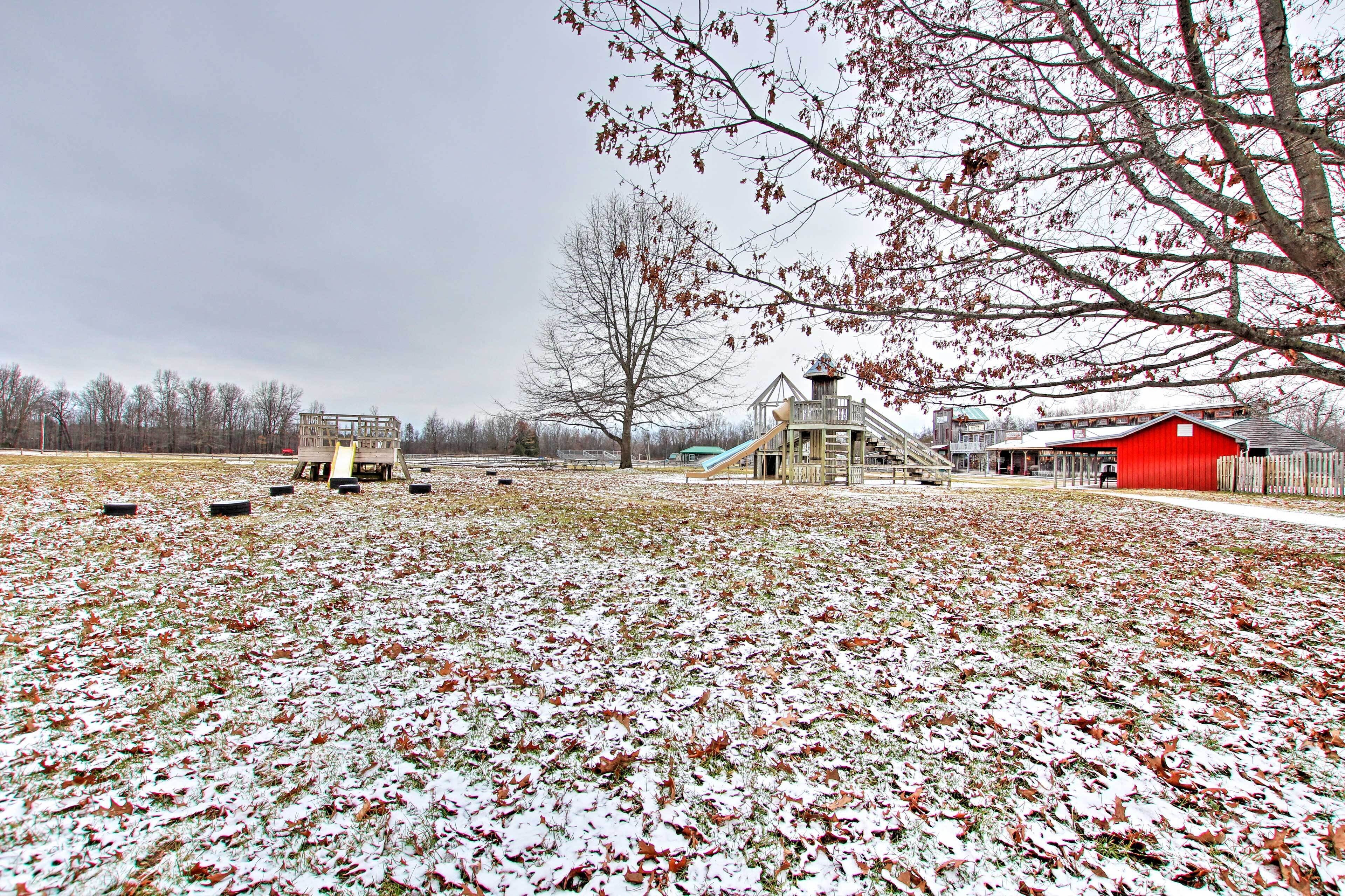 A playground with slides and climbing structures, a red barn, and a large tree in a rural setting.