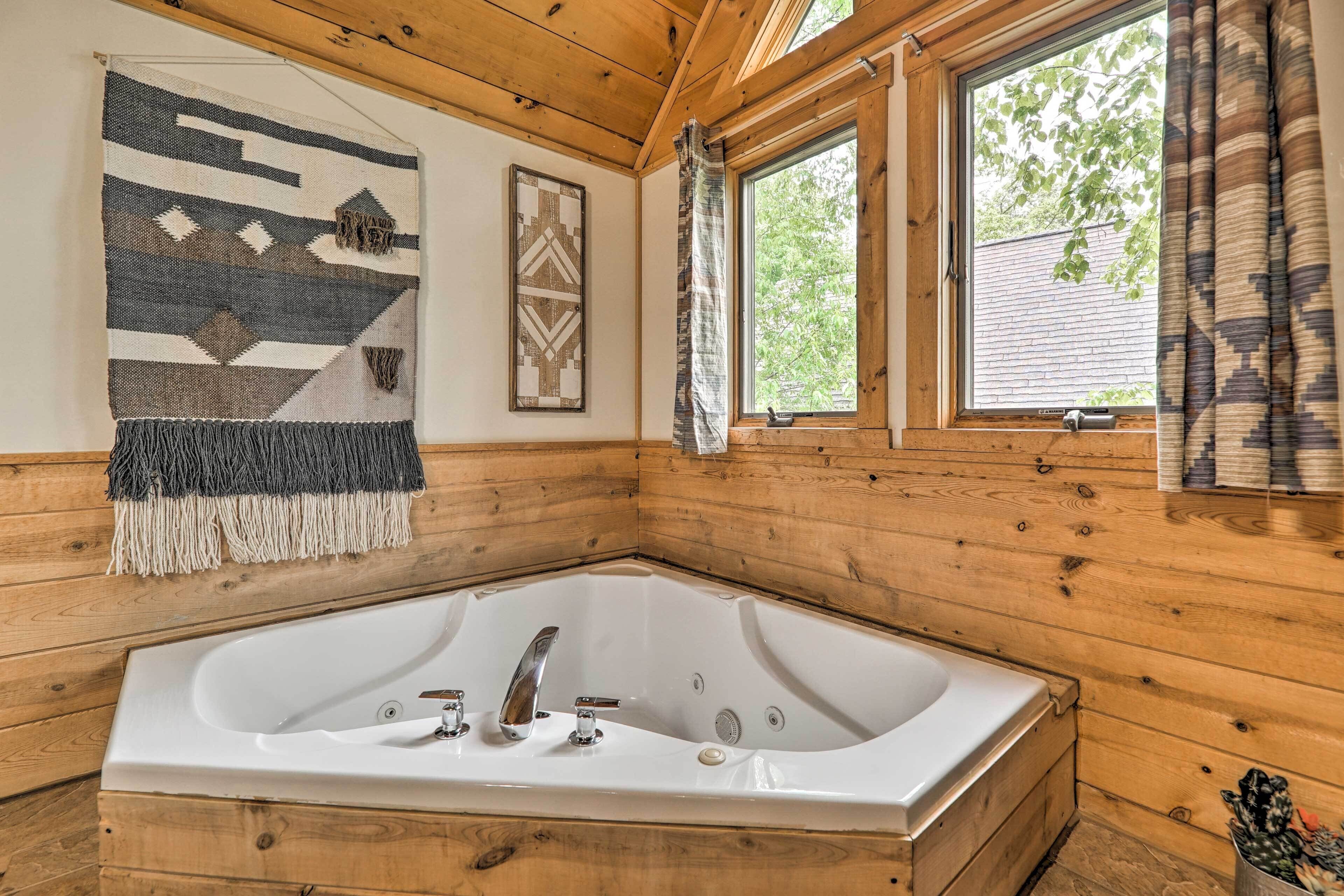 Ein Badezimmer einer Holzhütte mit einer großen Badewanne, Holzwänden, einem Fenster mit Vorhängen und einer Wanddekoration.