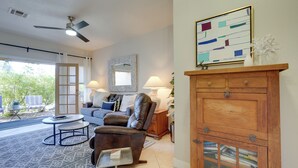 A living room with a sofa, armchair, and coffee table, a fireplace with books, and a view of greenery outside. - Scottsdale Home: Pool Access, 13 Mi to Phoenix (Scottsdale)