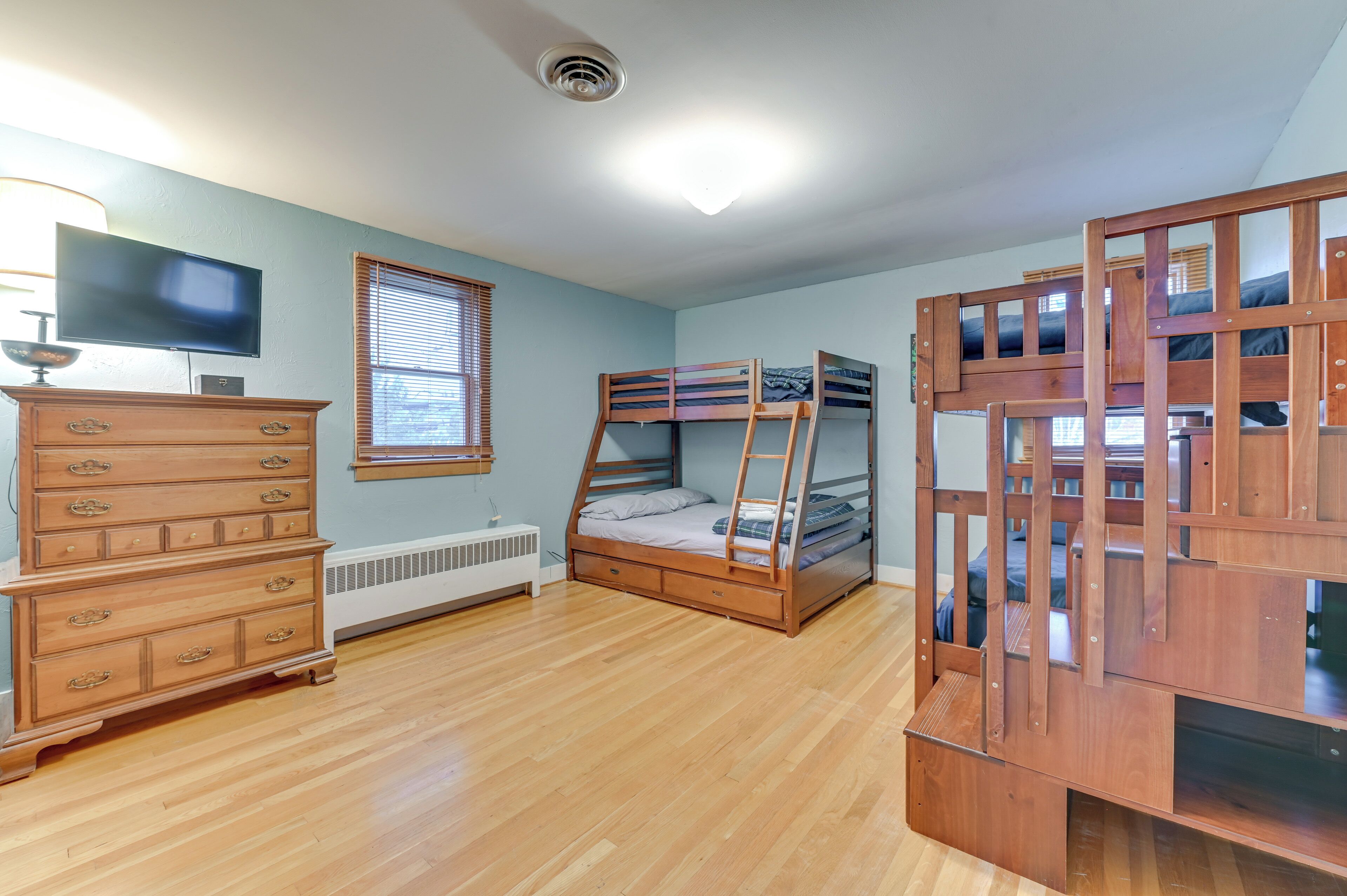 A room with a bunk bed, a dresser, a television, and a window with blinds.