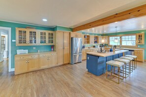 A spacious kitchen with wooden cabinets, a large island with bar stools, and a view of the outdoors through the windows.