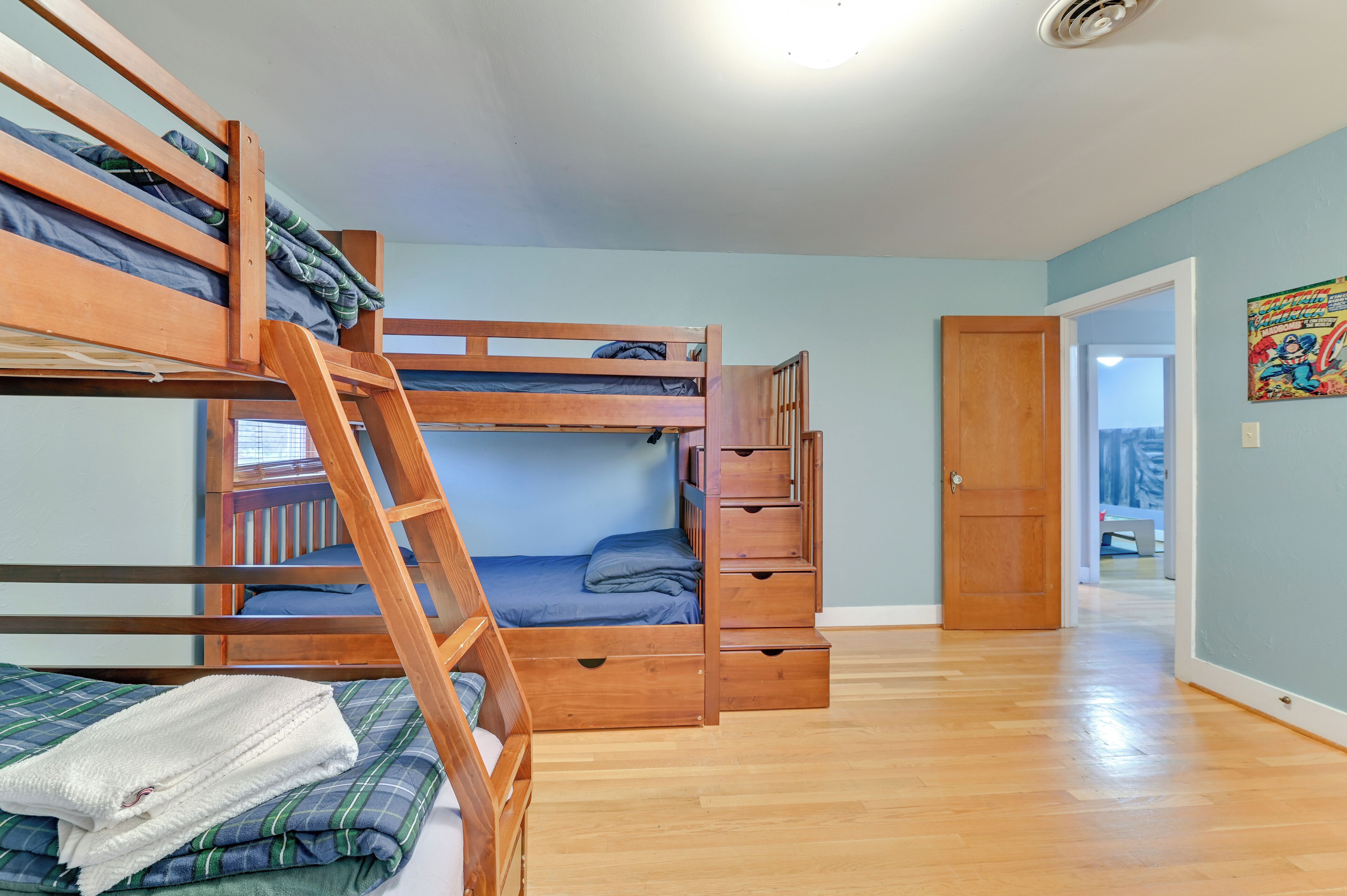 Une chambre avec un lit superposé, une échelle en bois, une porte et un couloir menant à une autre pièce.