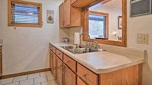 A kitchen with wooden cabinets, a stainless steel sink, and a large mirror above the counter. - Riverfront Elkins Home w/ Fireplace & Deck! (Elkins)