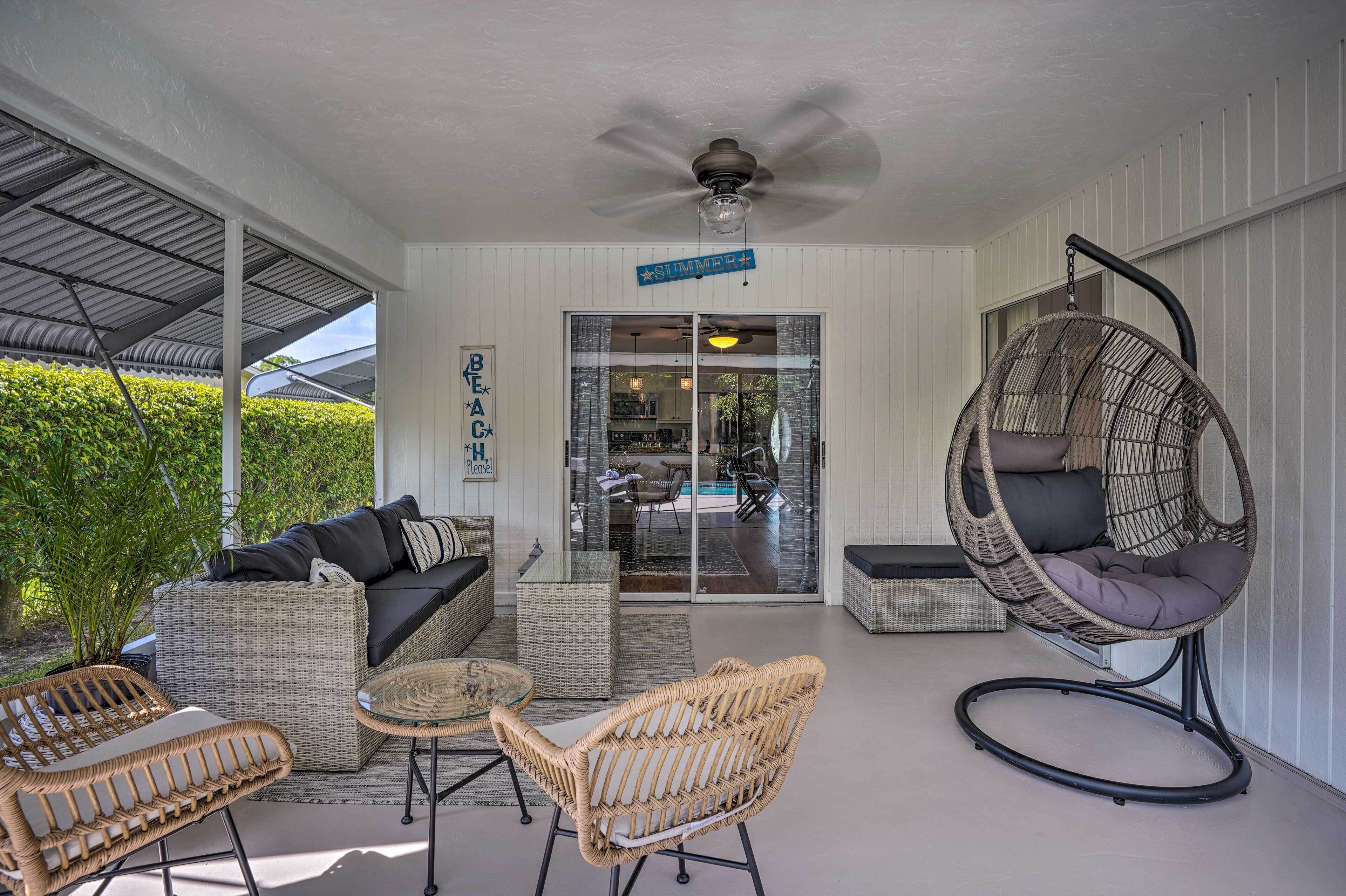 A covered outdoor seating area with wicker furniture, a ceiling fan, and a glass door leading to a pool.