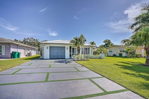 A residential driveway leading to a garage, surrounded by well-maintained lawns and palm trees.