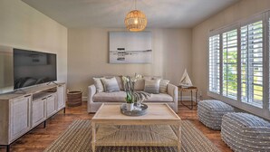 A living room with a television, sofa, coffee table, and large windows. - Naples Oasis w/ Screened Pool, Bike to Beach! (Naples)