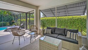 A sunlit indoor patio with a pool, wicker furniture, and a sofa with cushions. - Naples Oasis w/ Screened Pool, Bike to Beach! (Naples)