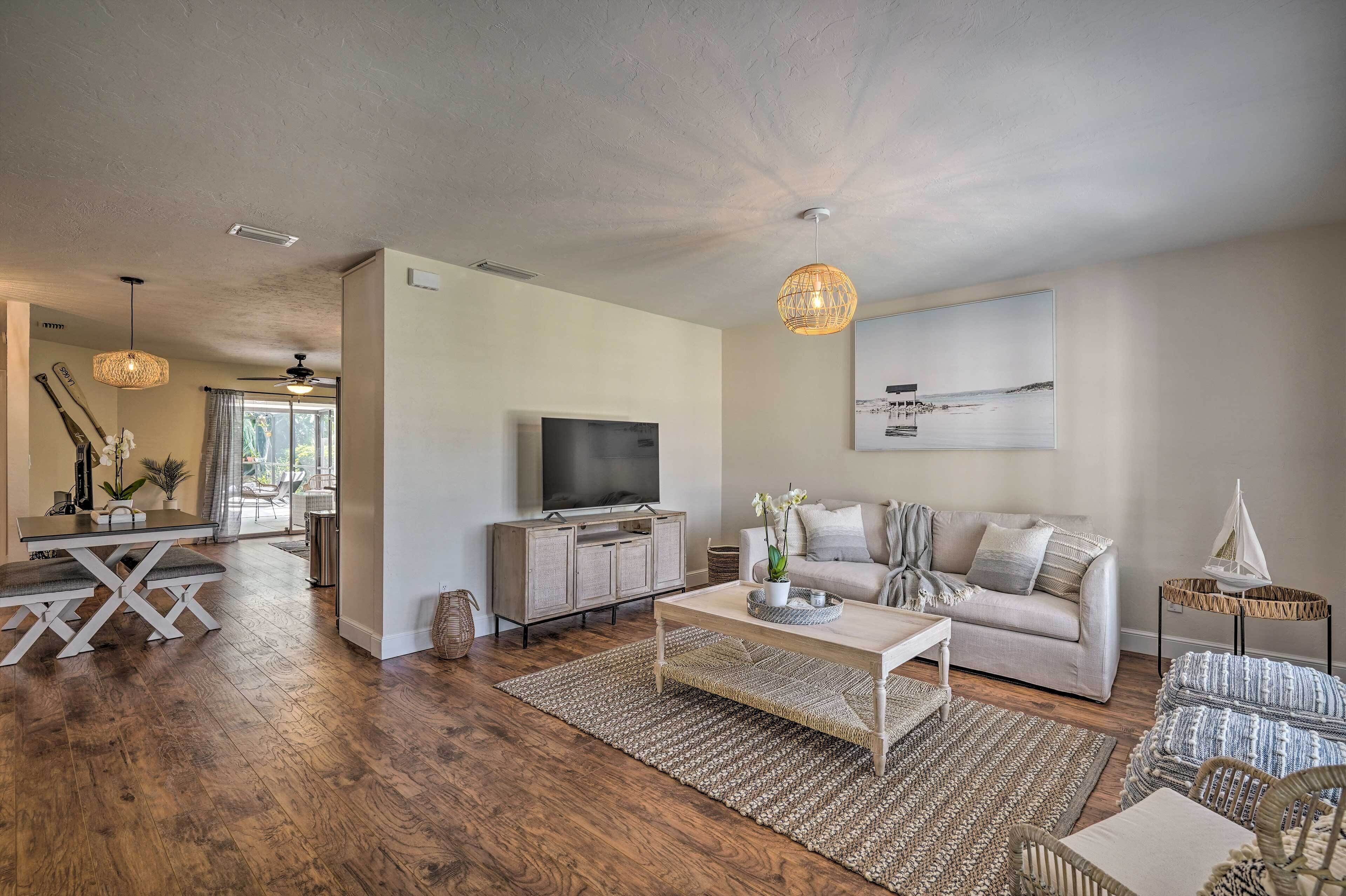 A modern living room with a sofa, coffee table, and TV. There is a dining area with a table and chairs.