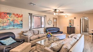 A living room with a glass coffee table, leather sofas, a painting, a clock, and a door leading to another room. - Lake Havasu City Home w/ Views: 3 Mi to Marina! (Lake Havasu City)