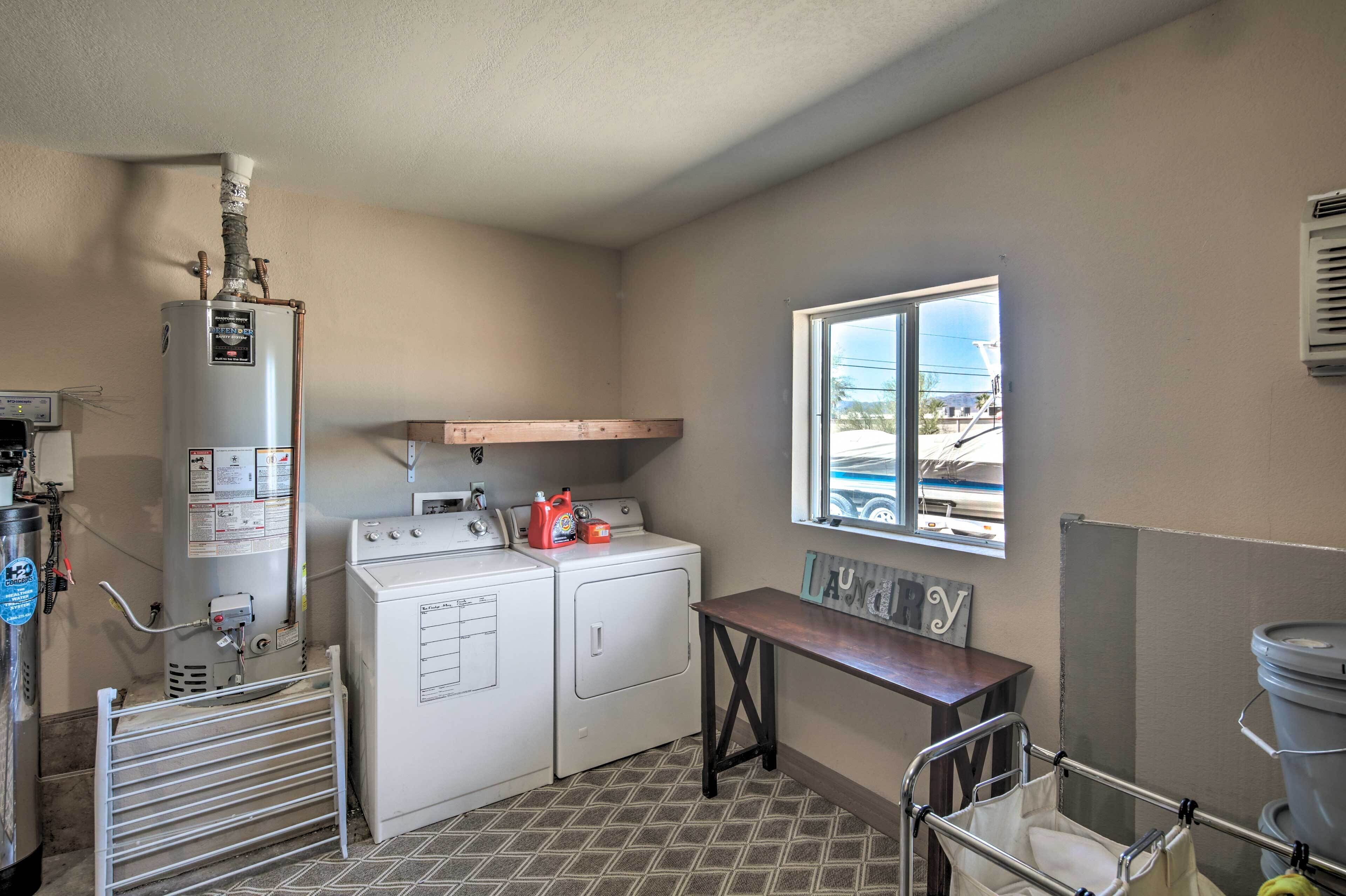 A laundry room with a water heater, washing machine, and dryer. There is a window with a view of buildings outside.