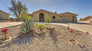 A residential building with a stucco exterior, a central arched entrance, and a landscaped front yard with various plants and flowers. - Lake Havasu City Home w/ Views: 3 Mi to Marina! (Lake Havasu City)