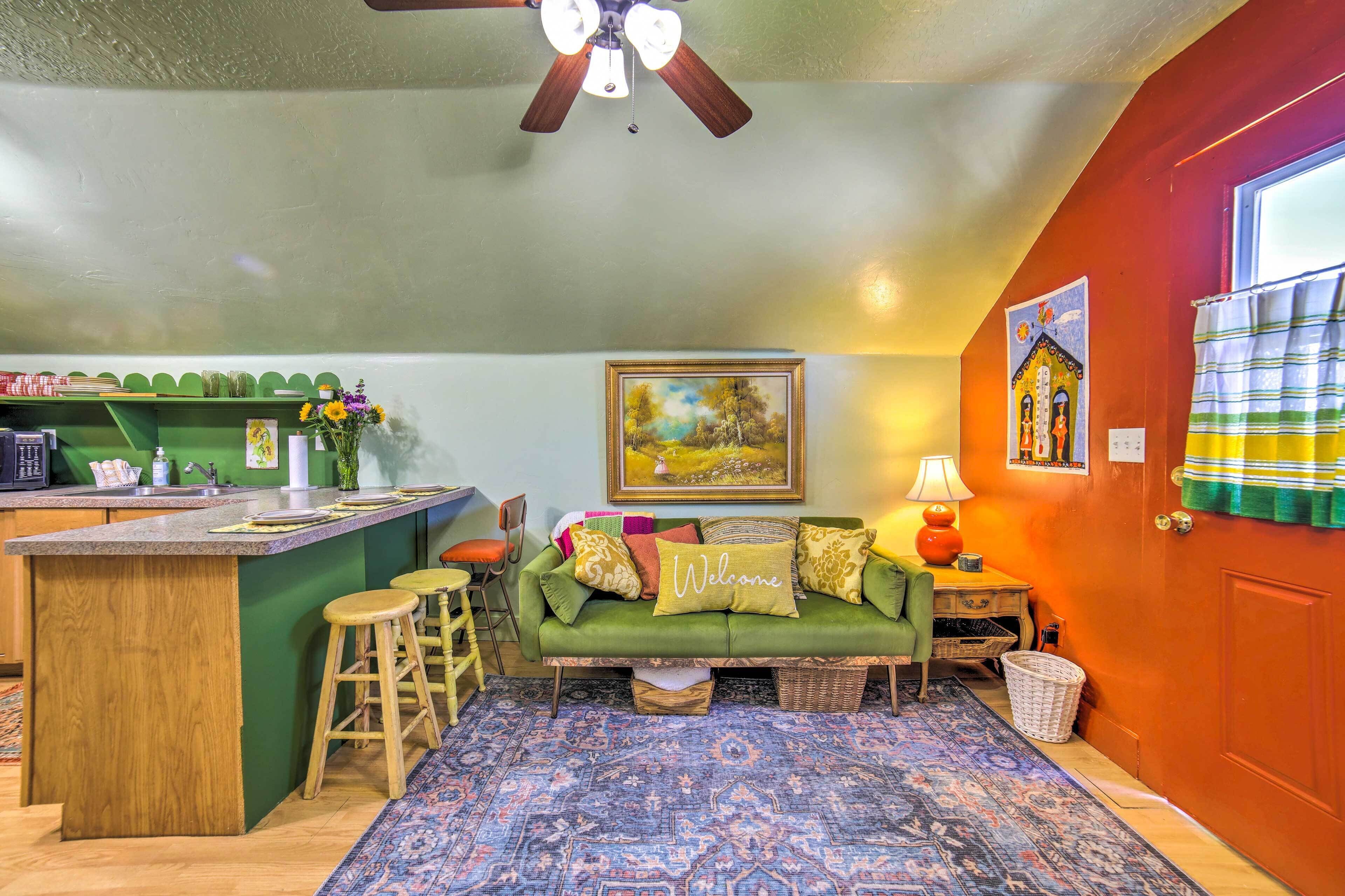 Una sala acogedora con un sofá verde, una pequeña zona de bar y un tapete estampado.