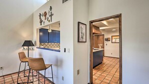 A hallway with a kitchen area, featuring a tiled floor, a bar area with stools, and a door leading to another room. - Beautiful 'saguaro Vista' w/ Mountain Views! (Tucson)
