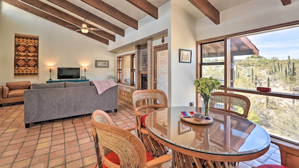 A spacious living area with a fireplace, a large window with a desert view, and a dining table with chairs. - Beautiful 'saguaro Vista' w/ Mountain Views! (Tucson)