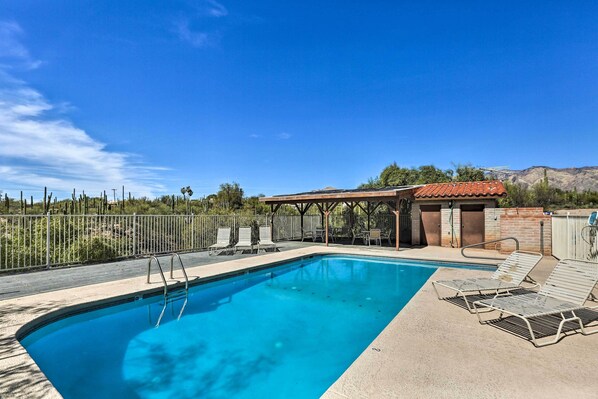 A rectangular swimming pool with a clear blue water, surrounded by a concrete deck. There are lounge chairs and a covered seating area with a red-tiled roof. - Beautiful 'saguaro Vista' w/ Mountain Views! (Tucson)