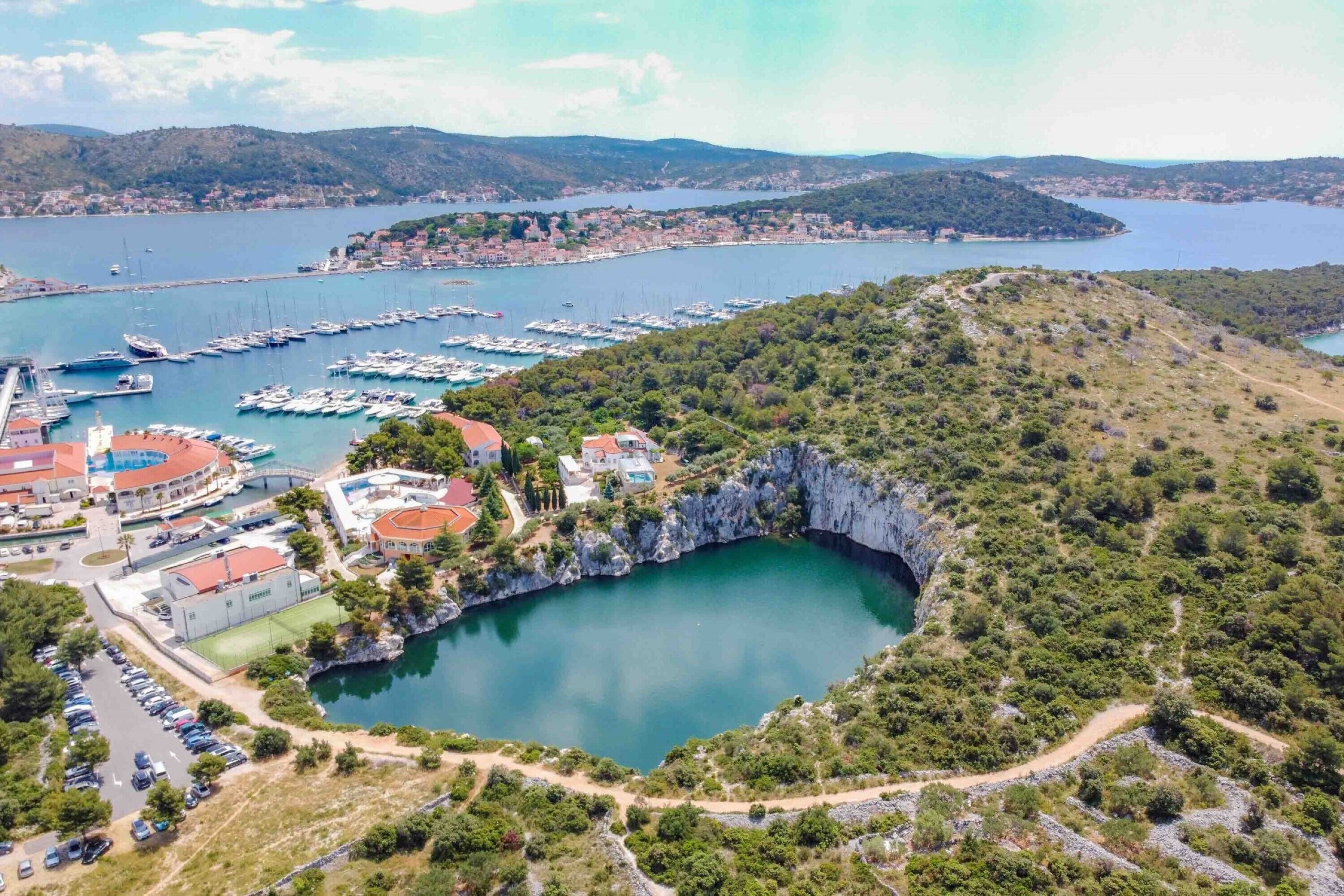 Zona costera con puerto deportivo, edificios y una formación rocosa natural.
