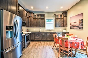 A modern kitchen with dark wood cabinets, stainless steel appliances, and a dining area with a red tablecloth. - Lakefront Home w/ Private Dock ~ 15 Mi to Walker (Walker)