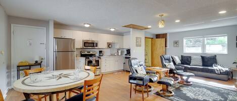 A modern kitchen with stainless steel appliances, a dining area with a round table and chairs, and a living area with a sofa and a coffee table.