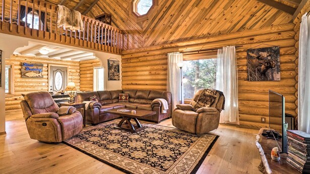 Ein Blockhaus-Interieur mit Holzbalkendecke, einem großen Teppich, Ledersofas und einem Esstisch.