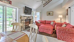 A cozy living room with a fireplace, a red patterned sofa, and a dining area with a table and chairs.