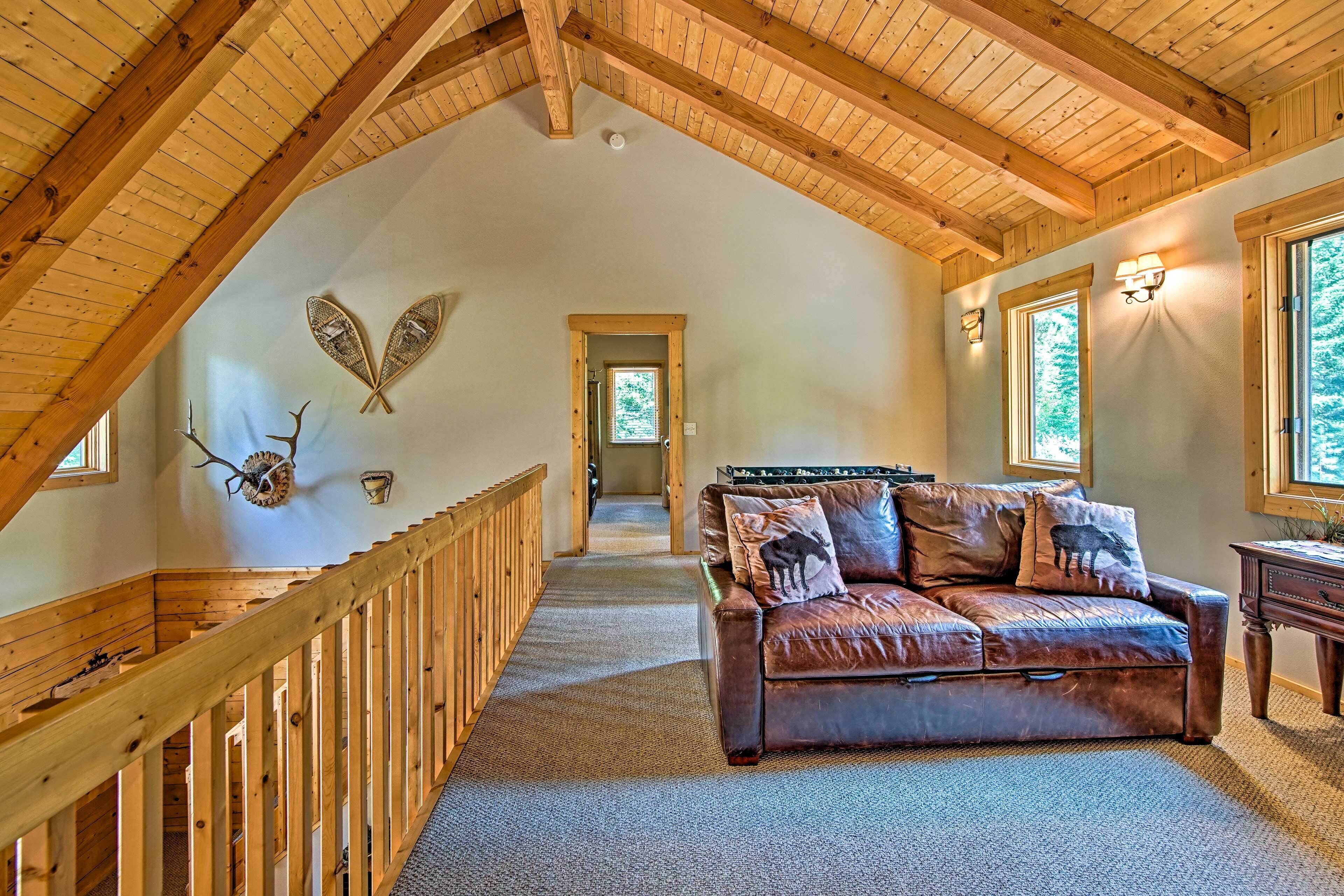 A spacious loft with a high ceiling, wooden beams, a leather sofa, and a staircase leading to another level.