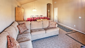 A living room with a sectional sofa, a dining table with chairs, and a hallway leading to a door. - 5 Mi to Spring Training: Family Home w/ Grill (Peoria)