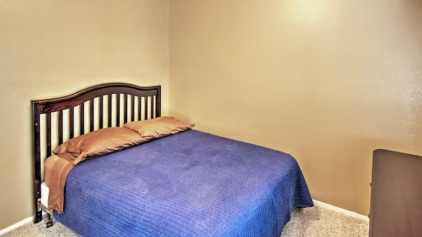 A single bed with a wooden headboard, a blue quilt, and two pillows in a room with beige walls. - 5 Mi to Spring Training: Family Home w/ Grill (Peoria)