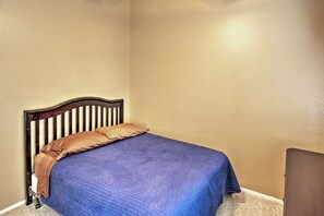 Un lit simple avec une tête de lit en bois, une couette bleue et deux oreillers, dans une pièce aux murs de couleur beige.