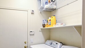A laundry room with two front-loading washing machines, a shelf with laundry supplies, and a door with a lock. - 5 Mi to Spring Training: Family Home w/ Grill (Peoria)
