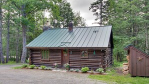 A log cabin with a metal roof, wooden door, and a small shed to the right. - Award-winning Log Cabin, Top 5 in New England! (Londonderry)