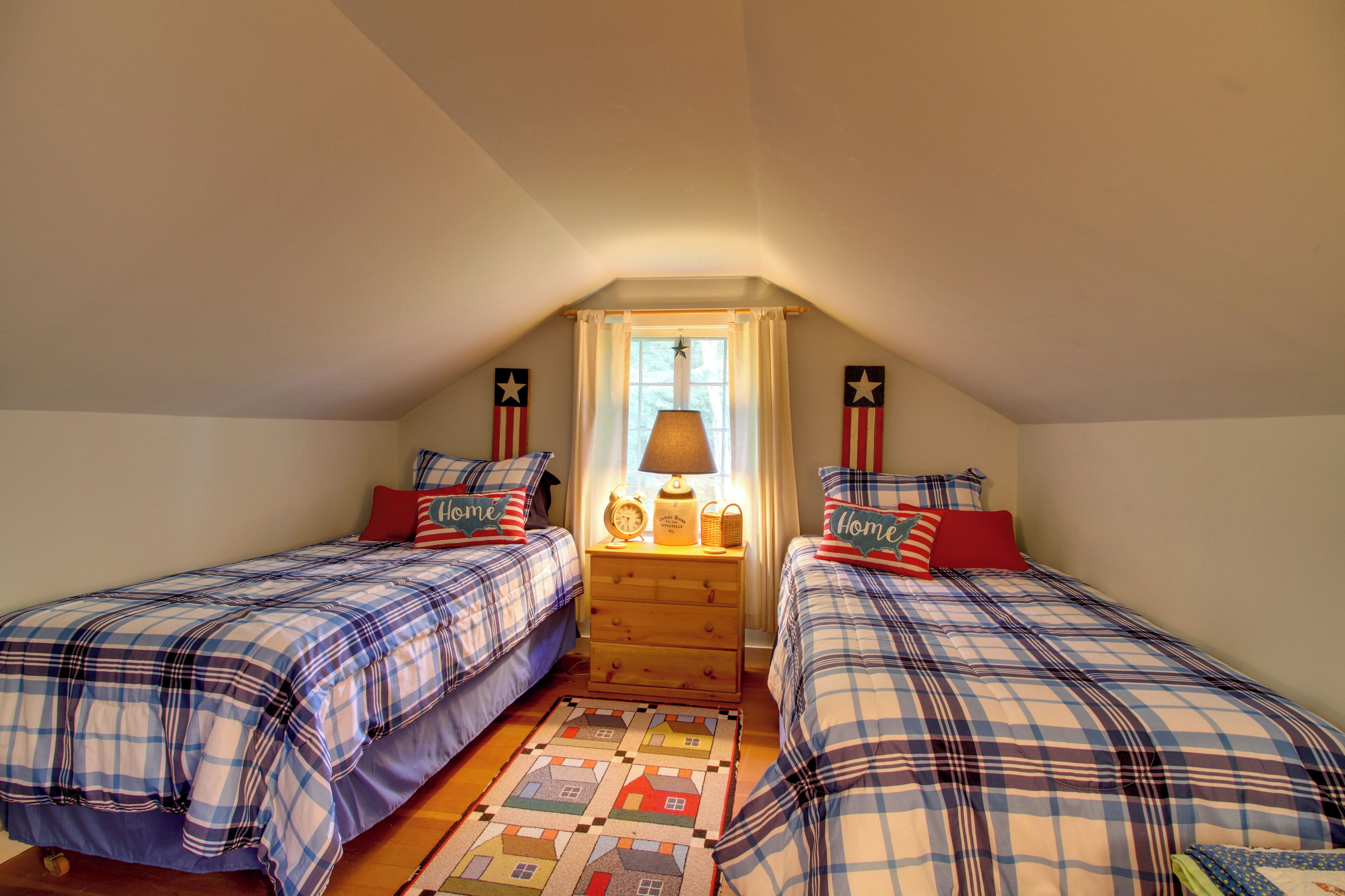 A bedroom with two beds, a nightstand, a lamp, and a quilted rug.