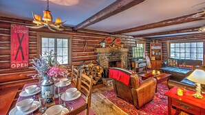 A cozy log cabin interior with a fireplace, wooden furniture, and a dining area. - Award-winning Log Cabin, Top 5 in New England! (Londonderry)
