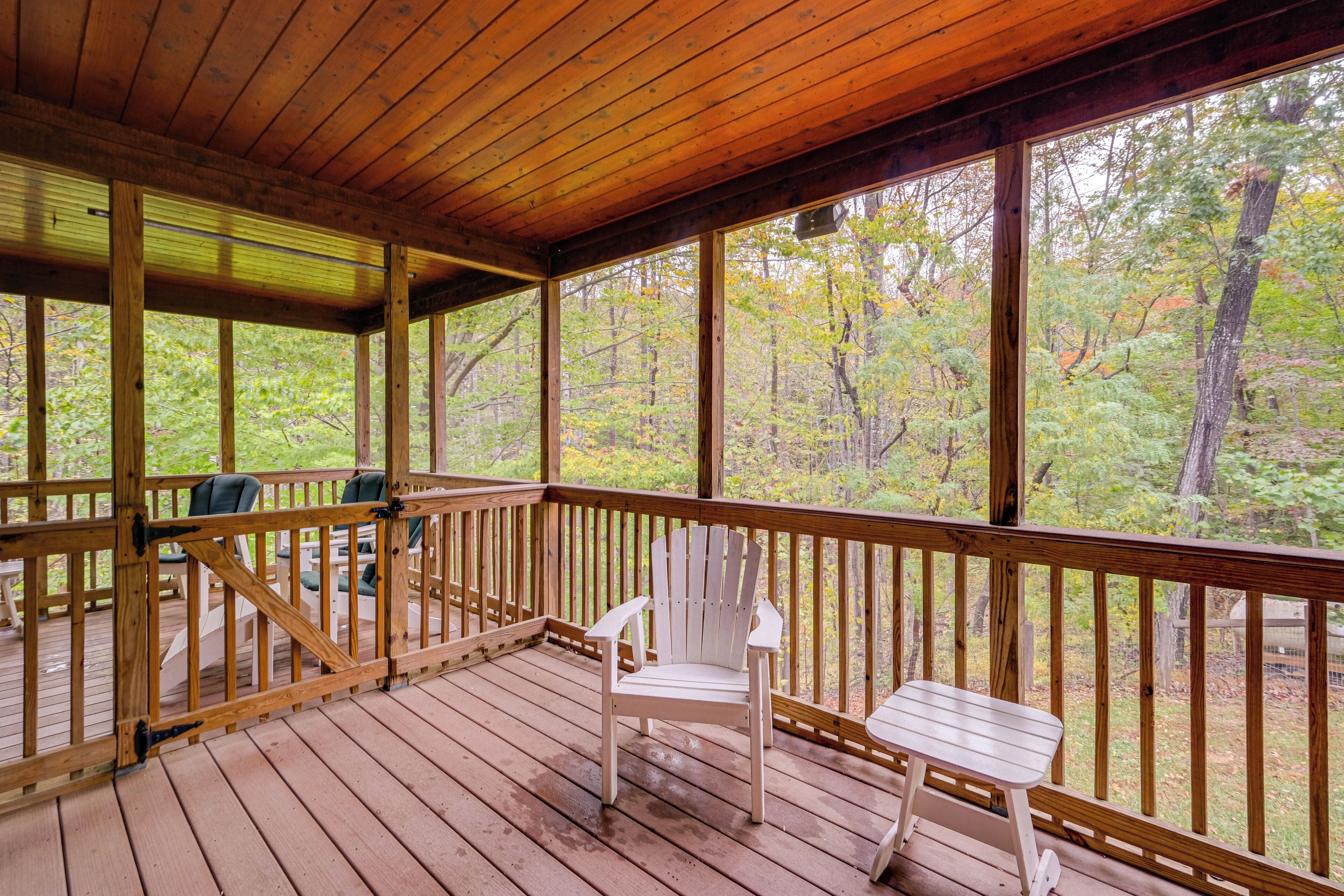 A wooden deck with a white chair and table, overlooking a forested area.