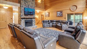 A spacious living room with a stone fireplace, leather sofas, and a large TV. - Spacious 5,200-sq-ft Cabin in Shenandoah Valley (Maurertown)