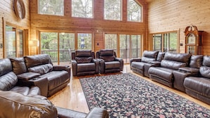 A spacious living room with leather sofas and armchairs, large windows, and a wooden interior. - Spacious 5,200-sq-ft Cabin in Shenandoah Valley (Maurertown)