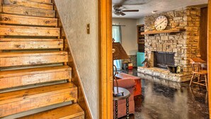 A wooden staircase leading to a living area with a stone fireplace, a clock, and a ceiling fan. - Wimberley Retreat w/ Grill < 2 Mi to Jacob's Well! (Wimberley)