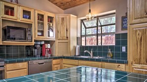 A kitchen with wooden cabinets, a microwave, a coffee maker, and a window with a view of trees. - 'hilda's Cabin' Mtn-view Retreat in Pine! (Pine)