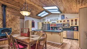 A cozy kitchen with wooden cabinetry, a dining area with a table and chairs, and a central island. - 'hilda's Cabin' Mtn-view Retreat in Pine! (Pine)