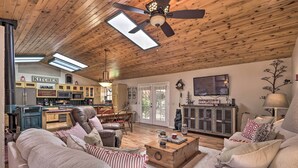 A cozy living room with a fireplace, a dining area, and a kitchen with wooden cabinets and a TV. - 'hilda's Cabin' Mtn-view Retreat in Pine! (Pine)