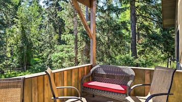 A wooden deck with wicker furniture and a red cushion, overlooking a forested area.